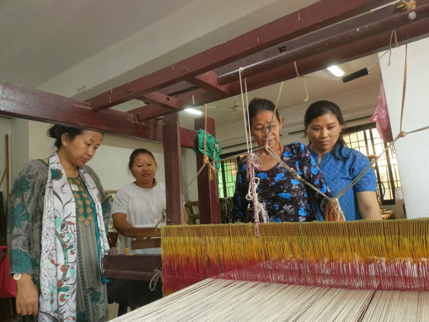 Trainees work closely with a Sabah Nepal trainer at a traditional loom, refining their weaving technique.